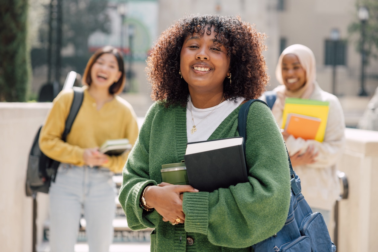 Three college girls smiling, holding books